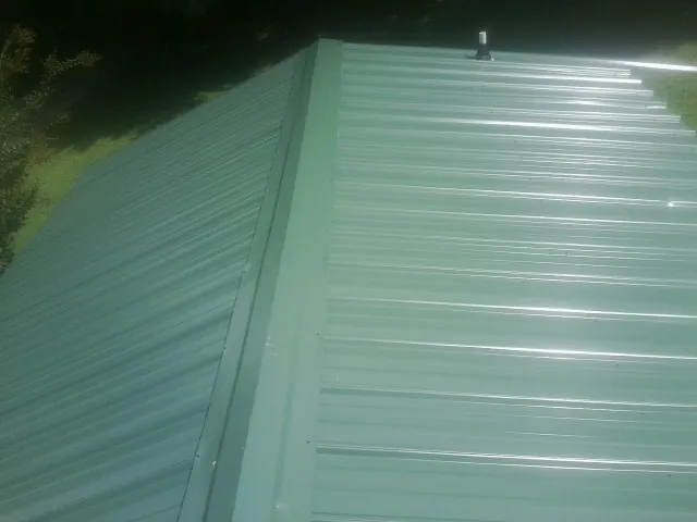 New green metal panels meeting at the ridge of a roof — Flat Roof Repair work by our crew in Arlington